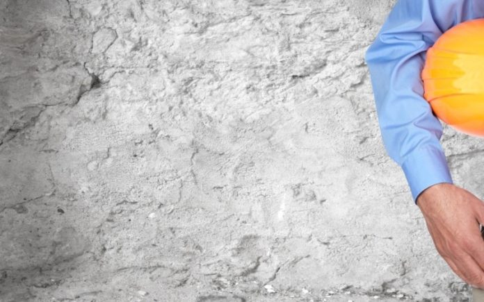 Construction worker with helmet over gray wall background.