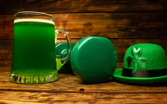 Heavy dumbbell, glass of green beer, Irish hat with shamrock leaf clover. Healthy fitness gym composition concept for St. Patrick's Day. Cheat day temptation vs sticking to the diet.