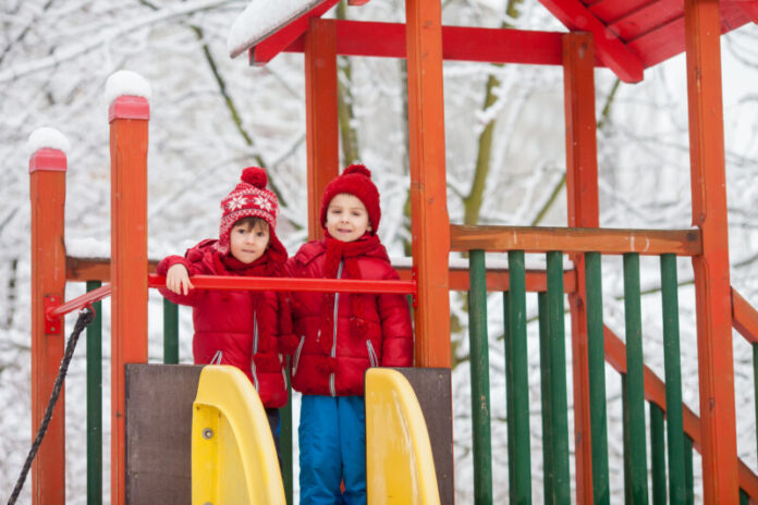Sweet children, playing in the snow on the playground Top Play Sets to Surprise Your Kids This Christmas